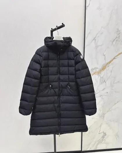 A long black quilted down coat on a hanger against a marble wall